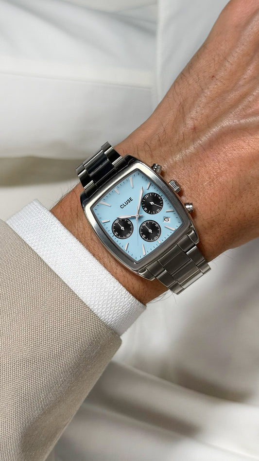 Silver watch on a wrist with a light blue face, worn against a neutral background.